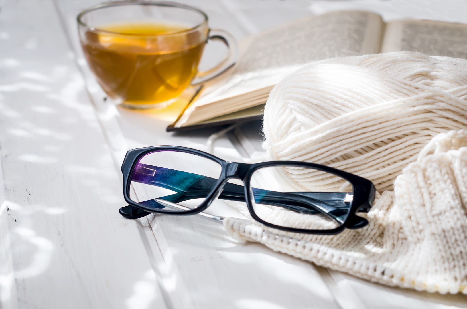 Lukulasit, kuppi teetä, kirja ja neulontavälineet